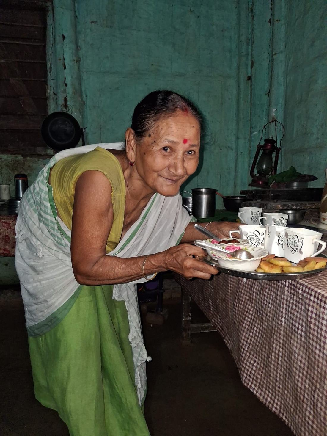 An elderly woman serving tea in a kitchen